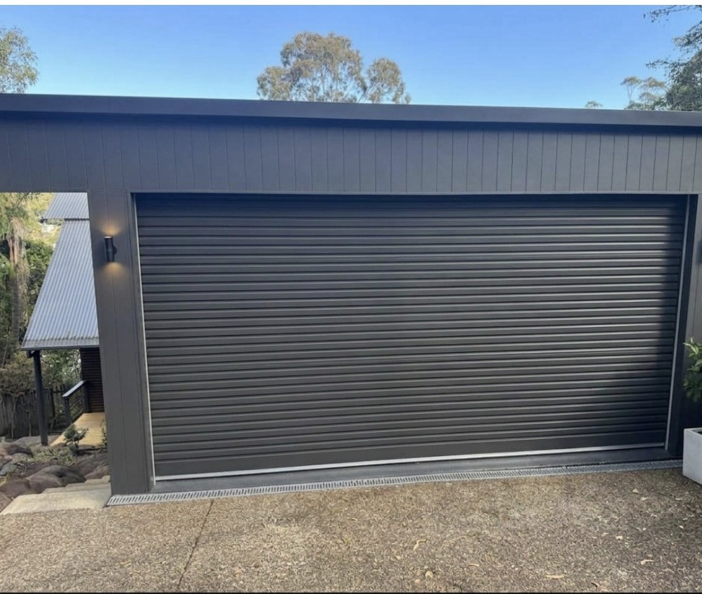 Dark clad garage with a wide roller door and a downlight