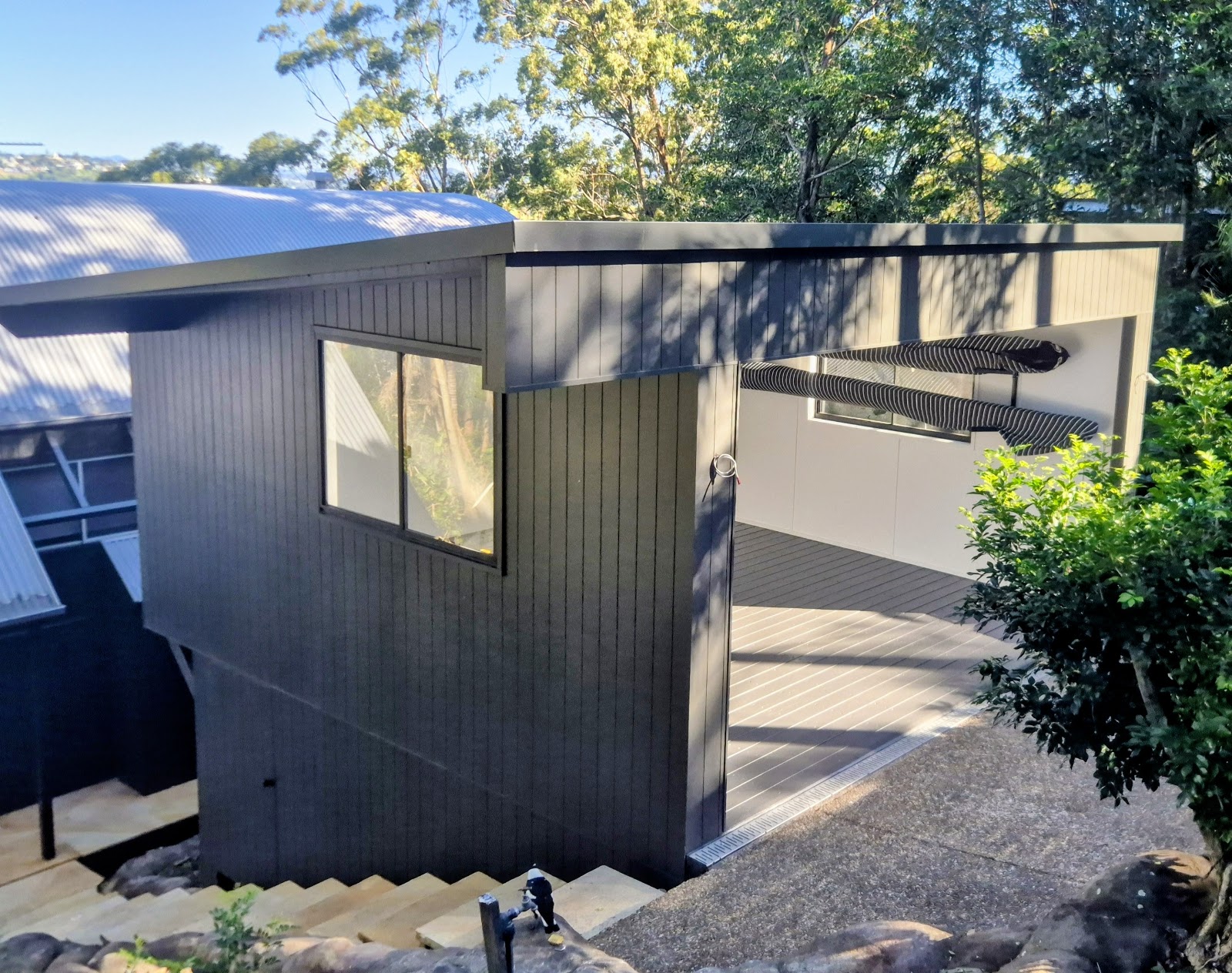 Dark vertical-groove clad studio extension with a covered deck on a sloping block